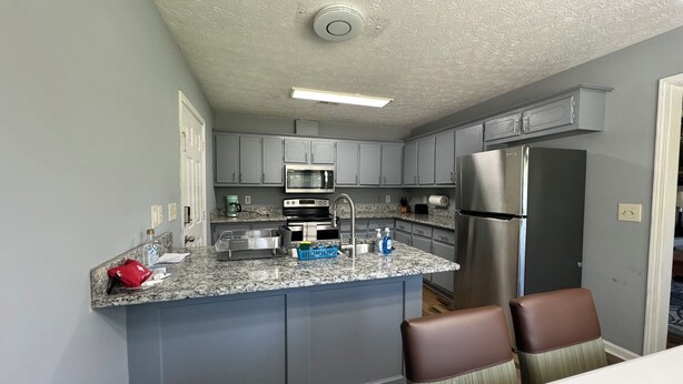 A modern kitchen with grey cabinets, a stainless steel refrigerator, and a granite countertop. - Joyful Place 2 King Bed 2 bath
10 Min to Berry College, Shorter University (Rome)