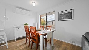 Een eethoek met een houten tafel en stoelen, een wit kastje en een raam met zonwering.