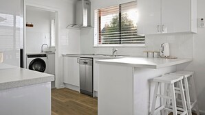 Een moderne keuken met witte kasten, een ingebouwde vaatwasser, een roestvrijstalen afzuigkap en een raam met jaloezieën.