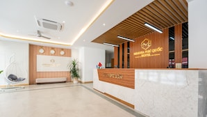 Ein Hotel-Empfangsbereich mit einem hölzernen Empfangsschalter, einer weißen gepolsterten Bank, einem Hängekorbstuhl und einem Blumentopf.