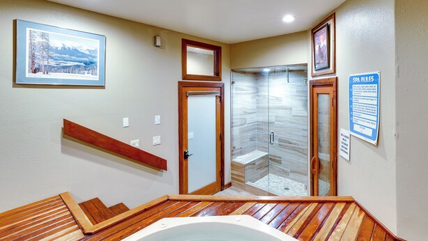 Un espace bien-être comprenant un jacuzzi, des marches en bois, une douche en verre et un tableau encadré au mur.