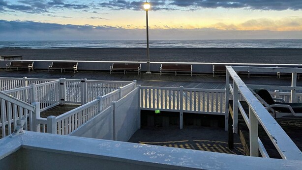 A deck with white railings overlooking a beach at sunset. - OCHG SeaFoam Ocean Front5 (Ocean City)
