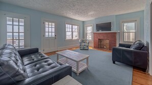 A living room with a fireplace, a sofa, a coffee table, and a patterned armchair. - OCHG SeaFoam Ocean Front5 (Ocean City)