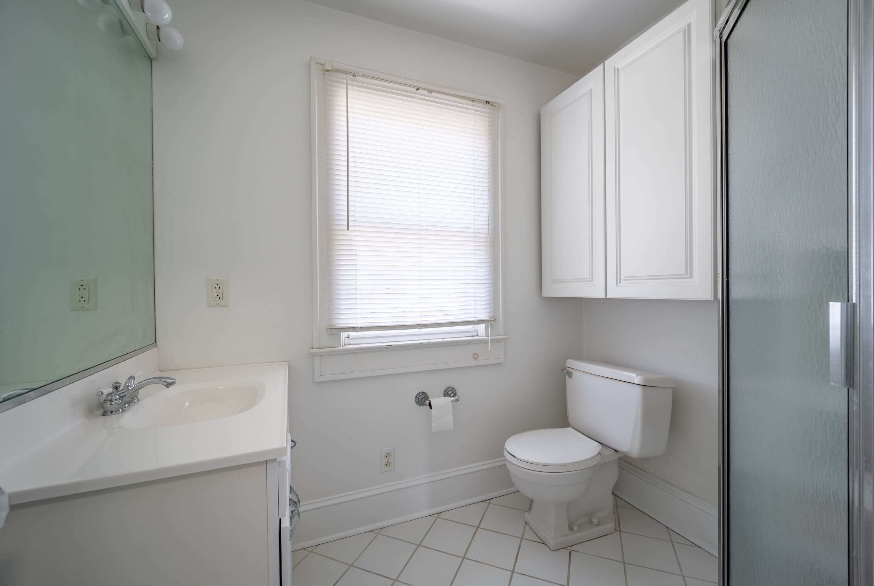 Ein Badezimmer mit weißem Waschbecken, Toilette und einem Fenster mit Jalousien.