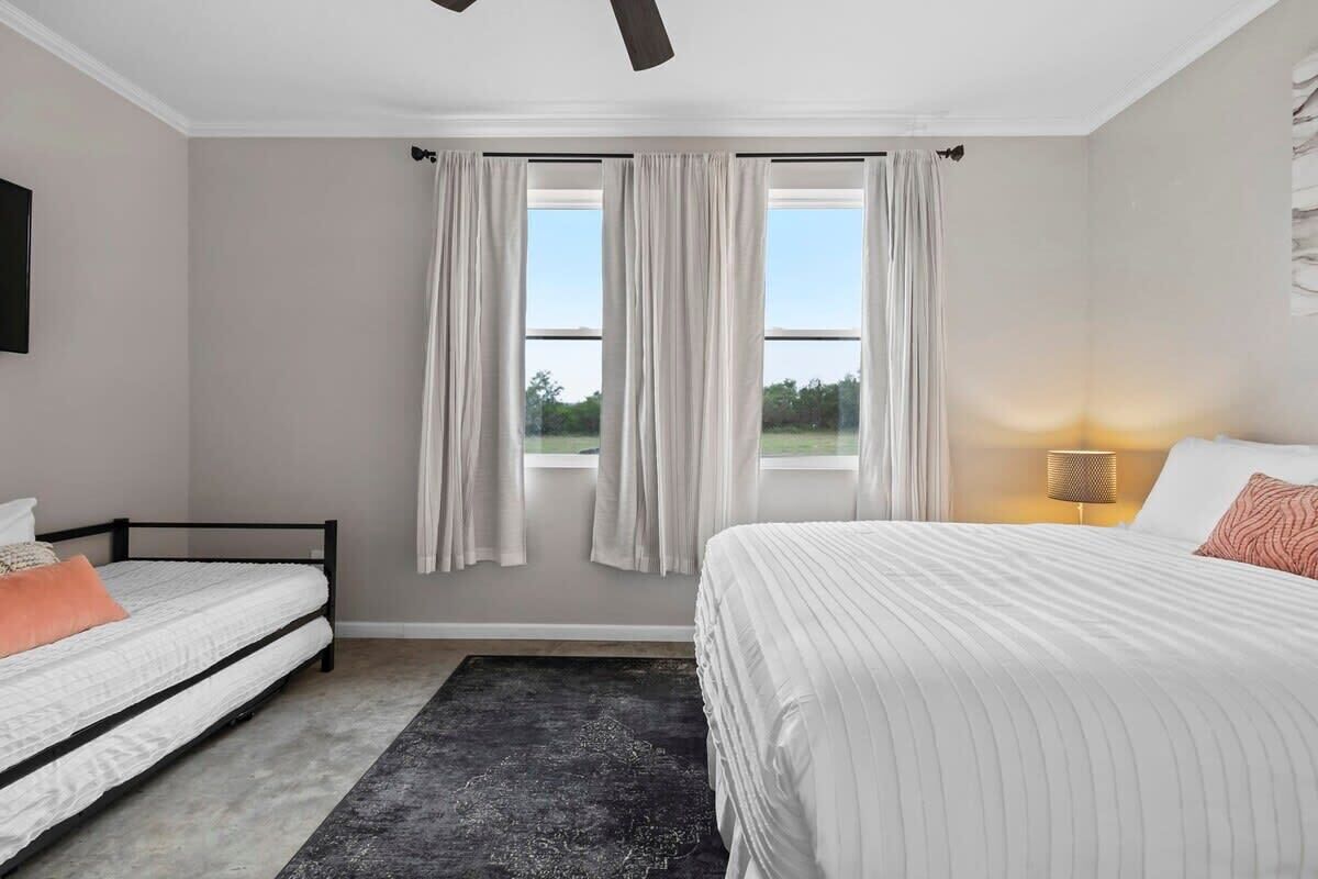 Une chambre à coucher avec un lit, une table de chevet, une lampe et une fenêtre avec des rideaux.