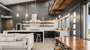 A modern kitchen with a central island, pendant lighting, and a dining area with a wooden table and chairs. - Enchanted Rock Ridge / Cowboy Pool / Hot Tub / Firepit (Fredericksburg)