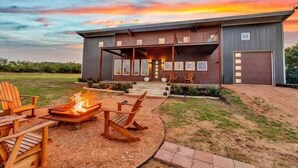 A modern house with a covered porch, a fire pit, and outdoor seating. - Enchanted Rock Ridge / Cowboy Pool / Hot Tub / Firepit (Fredericksburg)