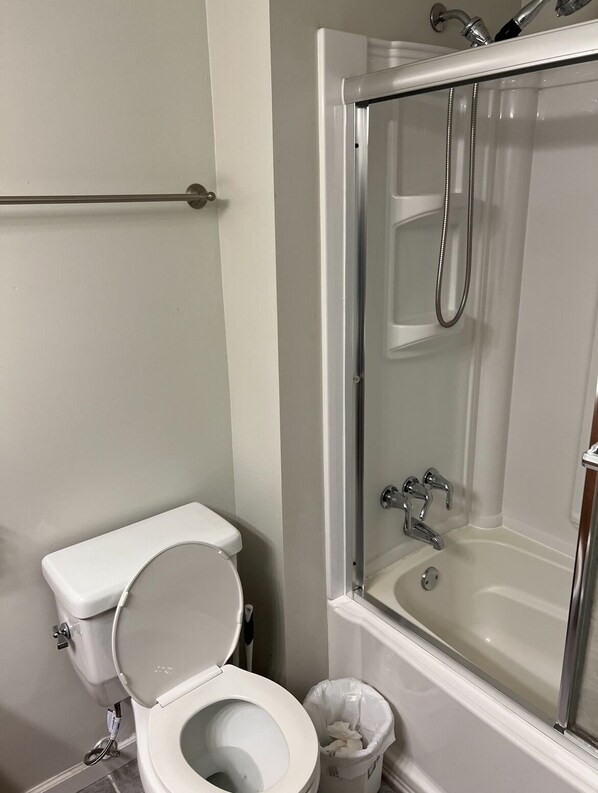 A bathroom with a toilet, a shower with a glass door, and a trash bin.