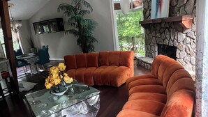 A spacious living room with a large orange sectional sofa, a glass coffee table with yellow flowers, a stone fireplace, and a ceiling fan.