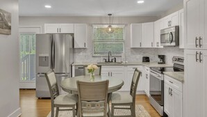 A modern kitchen with white cabinets, stainless steel appliances, and a dining area with a round table and chairs.