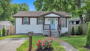 A single-story house with a front porch, mailbox, and a small garden with pink flowers.