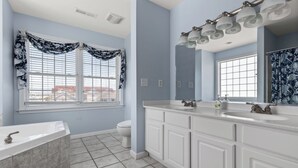 A bathroom with a large white vanity, a bathtub, and a window with floral curtains. - OCHG Townhouse 102 10 (Ocean City)