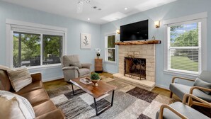 A living room with a fireplace, a ceiling fan, and a large TV mounted above it.