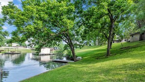 A serene lakeside setting with a grassy area, a small dock, and a building in the background.