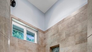 A shower with beige tiles, a window, and a mosaic floor.