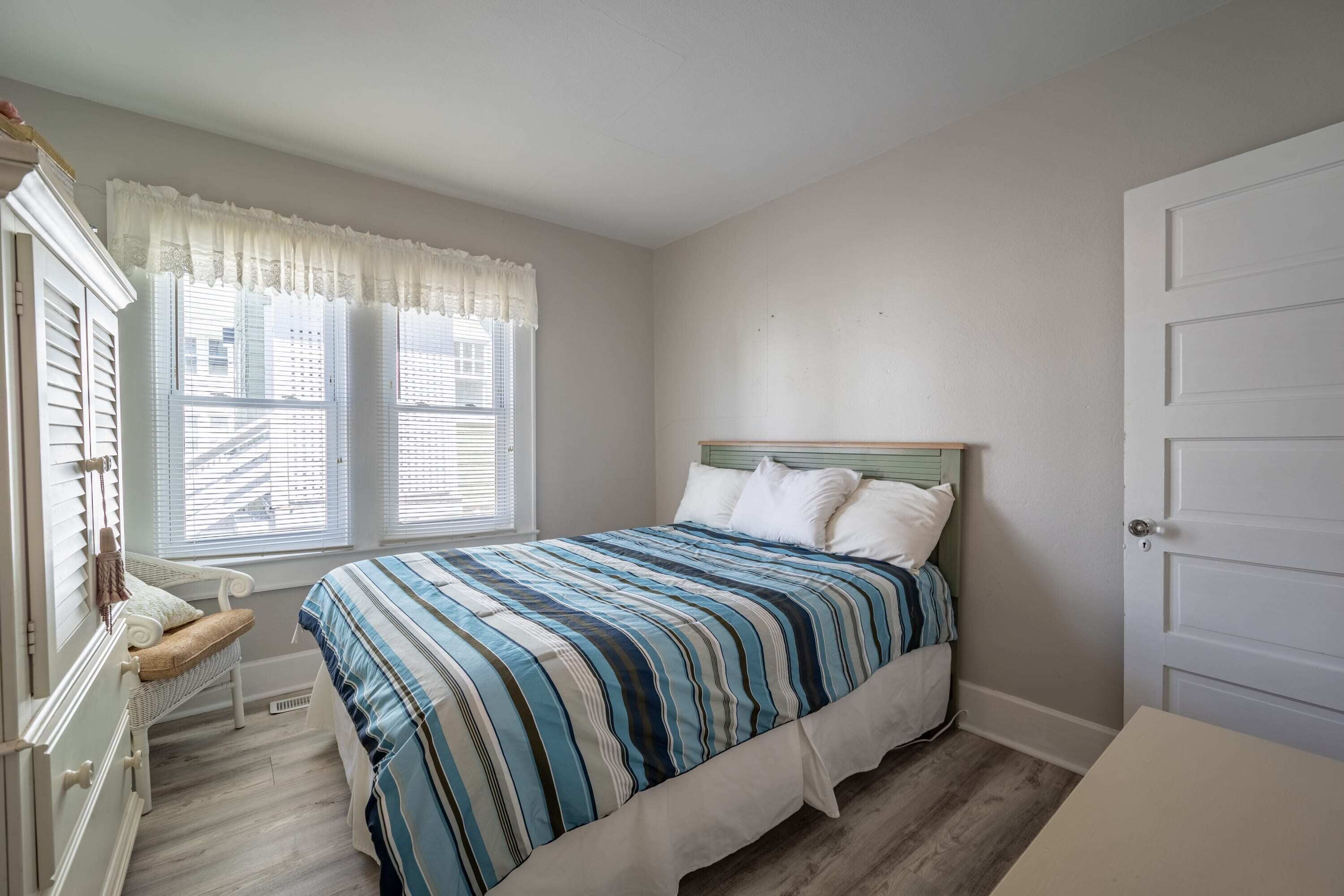 A bedroom with a bed, a window with blinds, a chair, and a door.