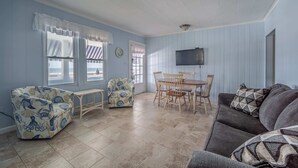 Een woonkamer met een bank, fauteuils, een eettafel met stoelen, en een aan de muur bevestigde televisie.
