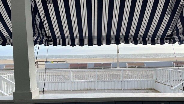 Uitzicht vanaf een balkon met een gestreepte luifel, op een strand met een houten omheining en banken.