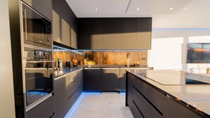 A modern kitchen with dark cabinetry, a marble countertop, and a geometric backsplash. - Villa Luxe by Atlantic Holiday (Ribeira Brava)