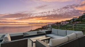 A balcony with wicker furniture overlooking a sunset over the sea. - Villa Luxe by Atlantic Holiday (Ribeira Brava)