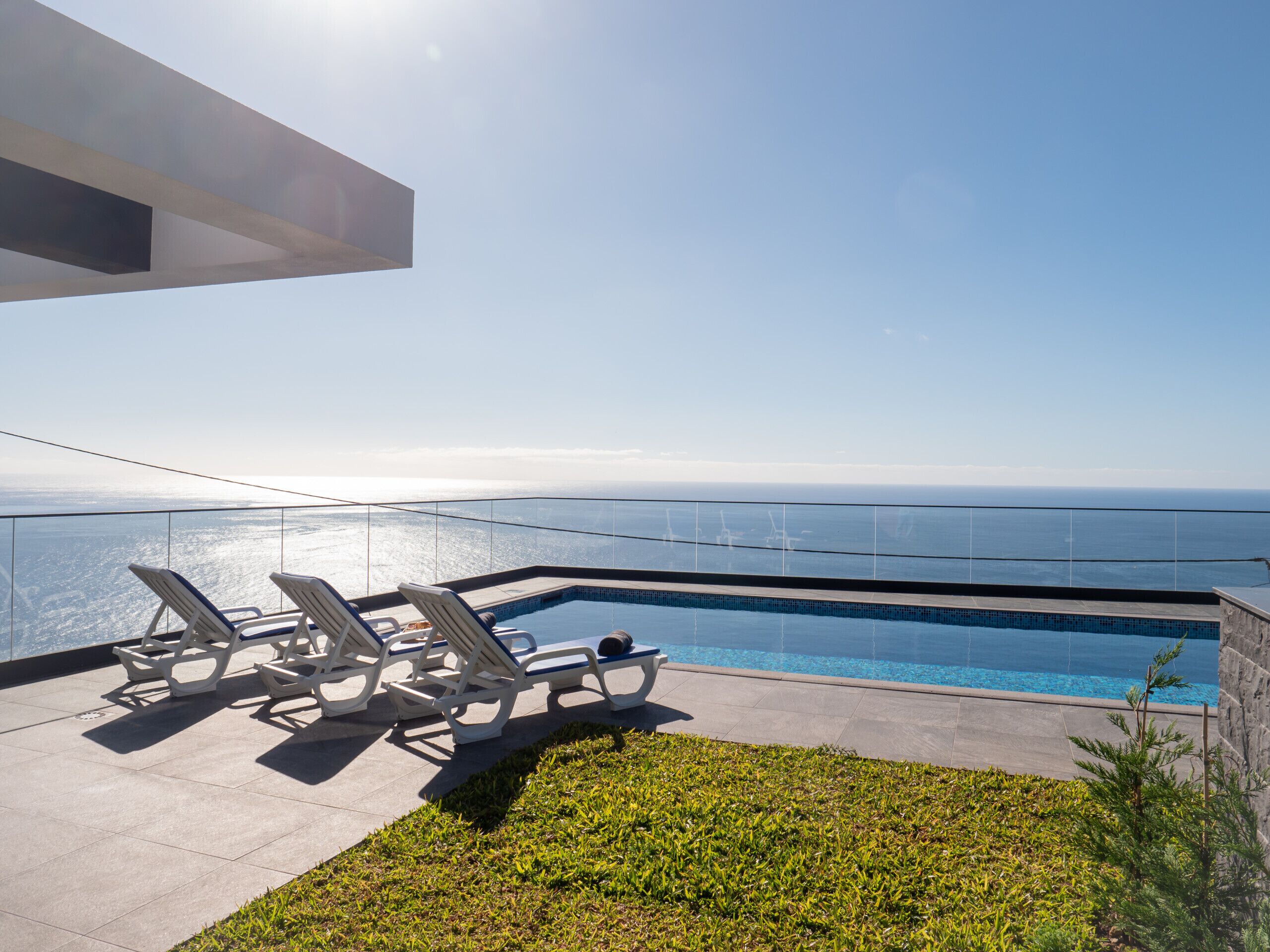 A modern outdoor pool area with lounge chairs and a clear view of the ocean.
