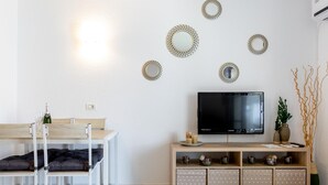Un salon moderne avec un téléviseur, une table à manger avec des chaises et des miroirs décoratifs sur les murs.