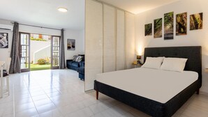Une chambre moderne avec un grand lit, un bureau et un canapé. Une porte coulissante donne accès à un balcon agrémenté de plantes.