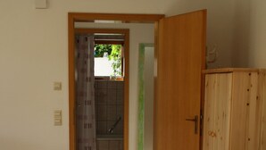 Une pièce avec une porte en bois, un canapé en cuir marron, un tapis blanc et, par une porte ouverte, on aperçoit une salle de bain.