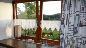 Une cuisine avec un plan de travail en bois, une fenêtre ornée de rideaux en dentelle et une vue sur un jardin.