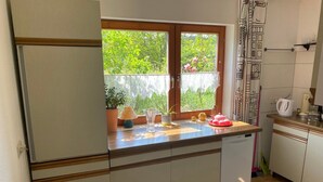 Une cuisine de taille réduite, dotée d’une fenêtre, d’un réfrigérateur, d’un évier et d’un plan de travail sur lequel sont disposés divers objets.