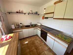 A kitchen with white cabinets, a wooden countertop, a stove, a sink, and a shelf with kitchen items. - Apartment 'Haus Sonnengarten' with Private Terrace, Garden and Wi-Fi (Seelbach)