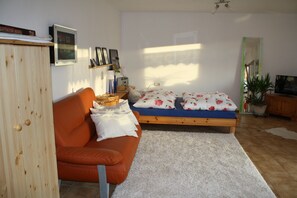 A room with a wooden wardrobe, a sofa, a bed with floral bedding, a small table with a lamp, and a potted plant. - Apartment 'Haus Sonnengarten' with Private Terrace, Garden and Wi-Fi (Seelbach)