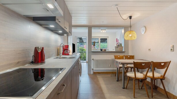 A modern kitchen with a built-in stove, a red kettle, and a dining area with wooden chairs. - Apartment 'Fewo Max' with Shared Terrace, Balcony and Wi-Fi (Ettenheim Münchweier)