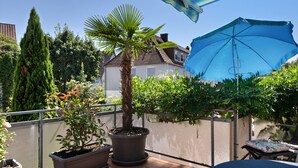 Ein Balkon mit Blumentöpfen, einem blauen Sonnenschirm und einem Stuhl.