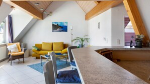 Ein modernes Wohnzimmer mit einem gelben Sofa, einem Essbereich mit einer Granit-Arbeitsplatte und einem großen Fenster mit Blick ins Freie.