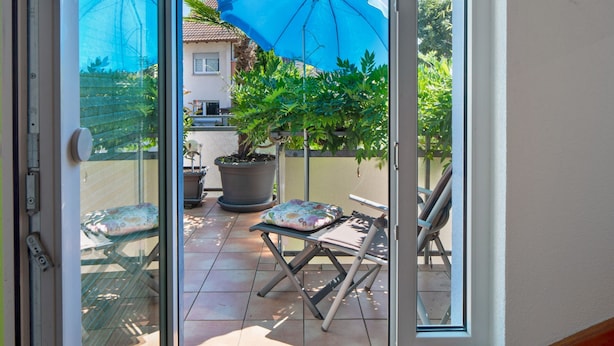 Eine Glastür führt zu einer Terrasse mit Tisch, Stühlen und einem Blumentopf.