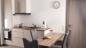 A modern kitchen with a wooden table, black chairs, a coffee maker, and a clock on the wall.