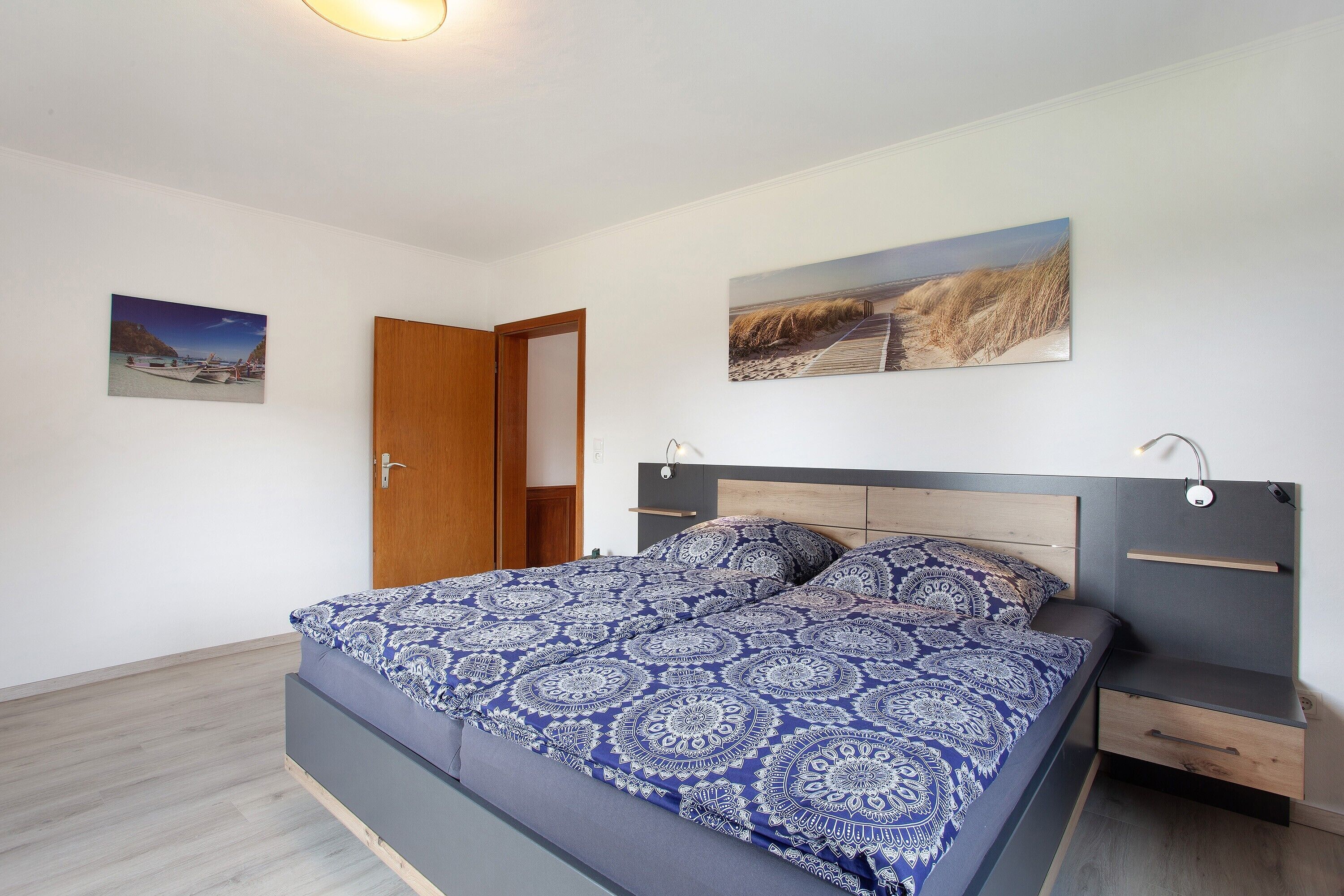 A bedroom with a bed, a nightstand, a drawer, and two wall-mounted pictures.