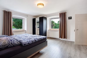 Une chambre à coucher avec un lit, deux fenêtres, une porte et un luminaire au plafond.