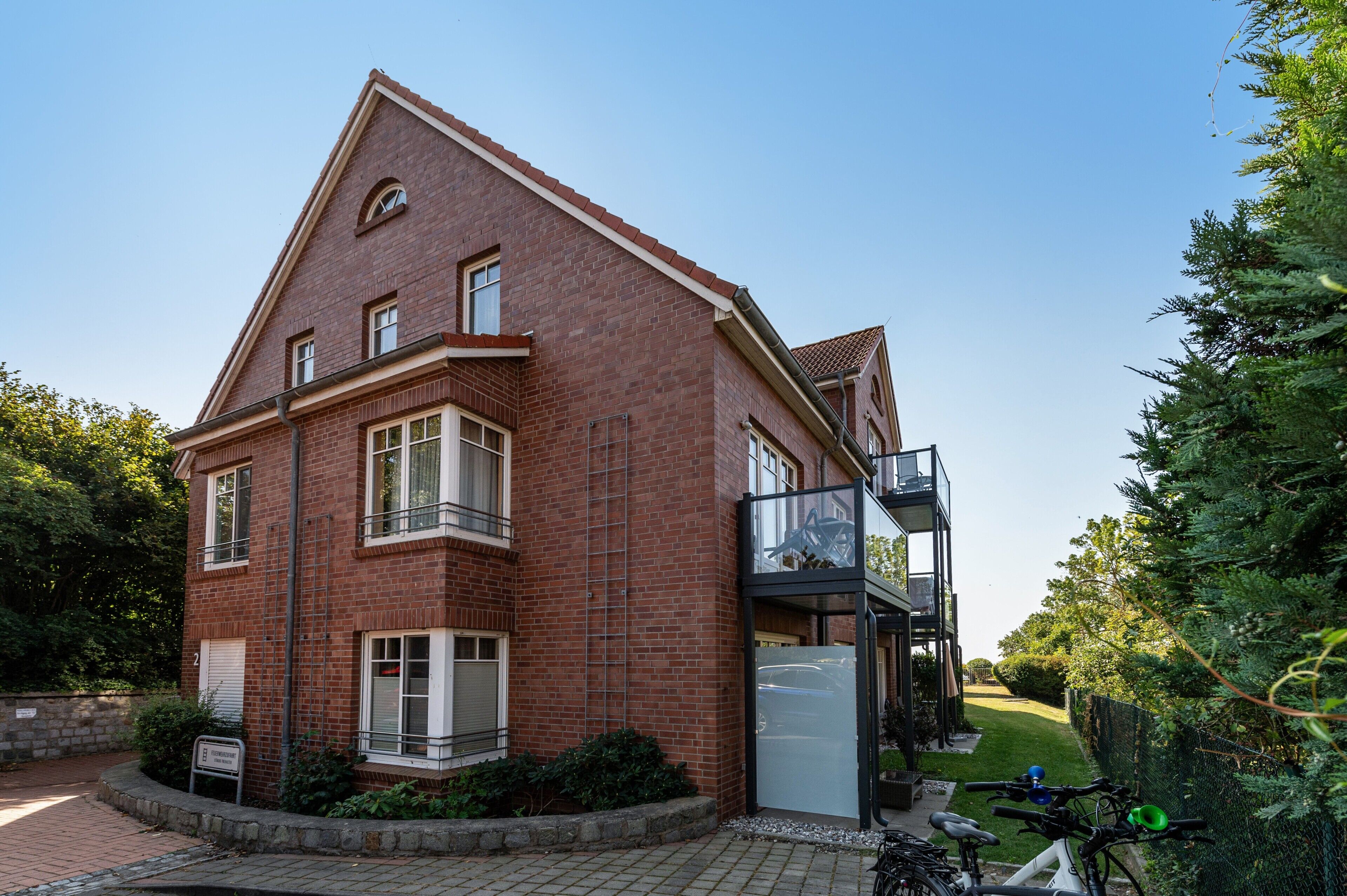Een rode bakstenen woning met een balkon, een garage en een verharde oprit.
