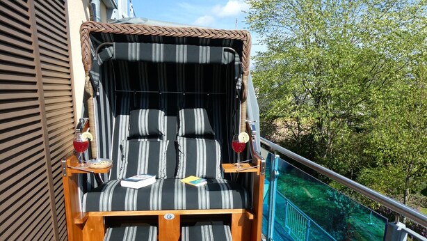 A sun lounger with striped cushions, a small table with a book and a drink, and a view of a blue slide and greenery. - Apartment 'Ferienwohnung Stella Fiante' with Sea View, Balcony and Wi-Fi (Breege-Juliusruh)