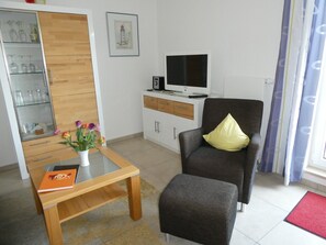 Una sala de estar con un sofá, una mesa de centro, un televisor y un mueble bar con cristalería.