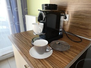 Una cafetera sobre una mesa de madera con una taza y platillo, una cuchara y un vaso.