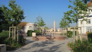 A courtyard with a central fountain, surrounded by trees and a building with a sign. - Apartment 'Ferienwohnung Stella Fiante' with Sea View, Balcony and Wi-Fi (Breege-Juliusruh)