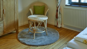 A room with a wicker chair, a radiator, a window with curtains, and wooden flooring.
