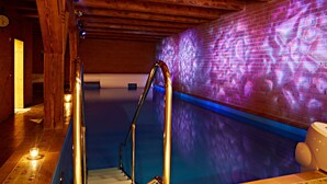 A swimming pool with a glass barrier, wooden beams, and a brick wall with a light projection.