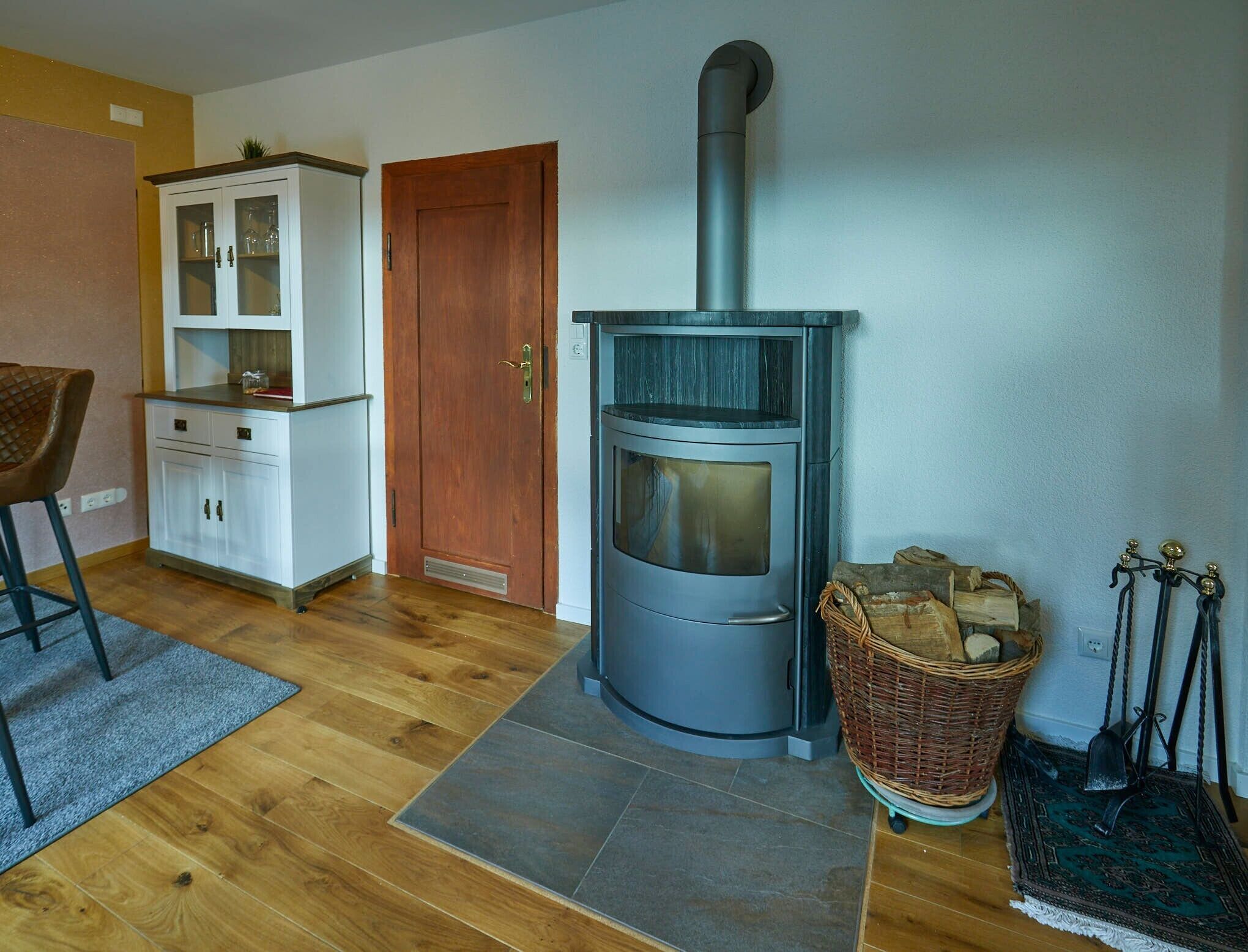 A cozy room with a wood-burning stove, a cabinet, a door, and a wicker basket with firewood.