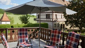 A balcony with outdoor seating, a large umbrella, and a traditional building in the background.