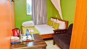 A room with a bed, a sofa, a table with a kettle, cups, and a bottle. - shammah hotel ltd (Kisumu)