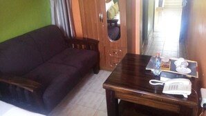 A room with a dark-colored sofa, a wooden table with a telephone and a bottle, and a small chair. - shammah hotel ltd (Kisumu)